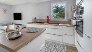 Eine moderne Küche mit weißen Schränken, einer Holzarbeitsplatte, einem großen Fenster und einem angebrachten Fernseher.