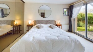 Ein Hotelzimmer mit einem großen Bett, zwei Nachttischen mit Lampen, einem runden Spiegel an der Wand und einem Fenster mit Vorhängen.