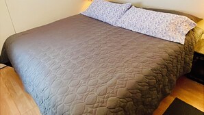 Una cama individual con cabecera acolchada, un cuadro en la pared y una lámpara de noche.