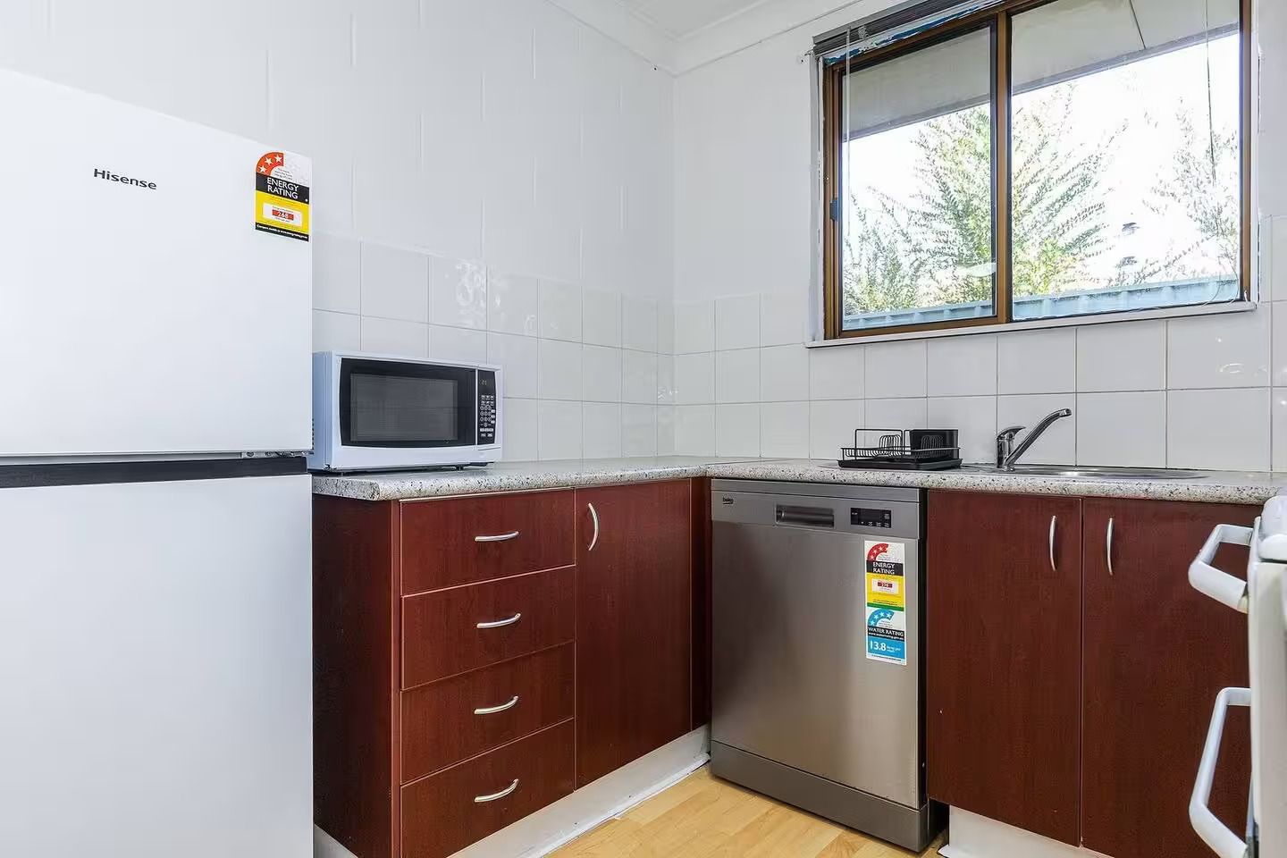 A compact kitchen with a microwave, dishwasher, and a window with a view of trees.