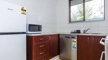 A compact kitchen with a microwave, dishwasher, and a window with a view of trees.