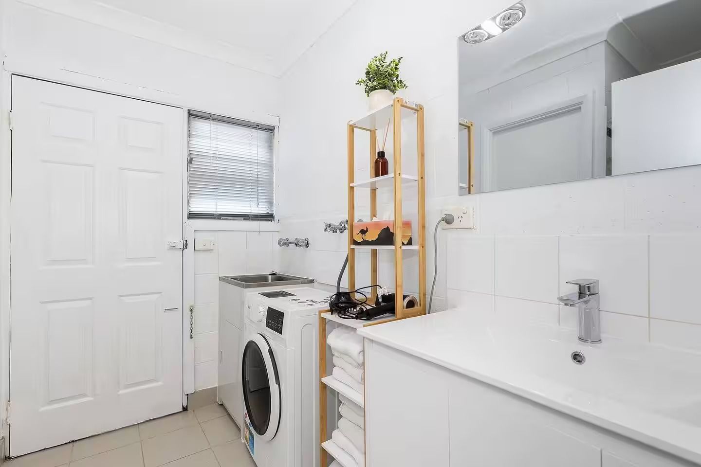 Ein kleines, modernes Badezimmer mit einer Waschmaschine, einem Waschbecken und einem Holzregal mit einer Pflanze.