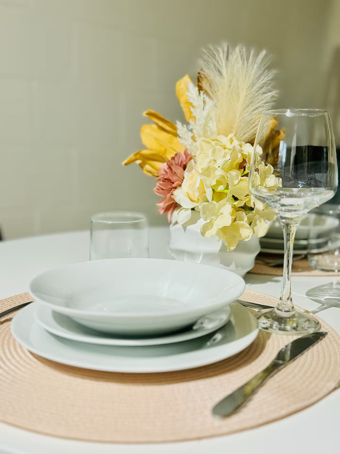 Une table dressée avec de l’assiette blanche, un verre d’eau et un arrangement floral au centre.