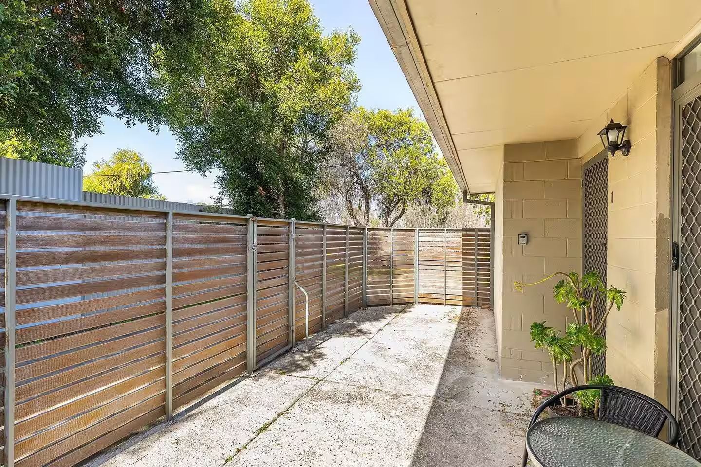 A covered patio area with a metal fence, a concrete floor, and a potted plant.