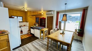 Une cuisine de taille réduite, dotée de meubles en bois, d’une table à manger et d’une fenêtre donnant sur les arbres.