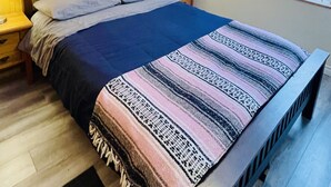 Une chambre à coucher avec une tête de lit en bois, un lit recouvert d’une couverture à motifs, une table de chevet avec une lampe et une fenêtre laissant entrer la lumière du jour.