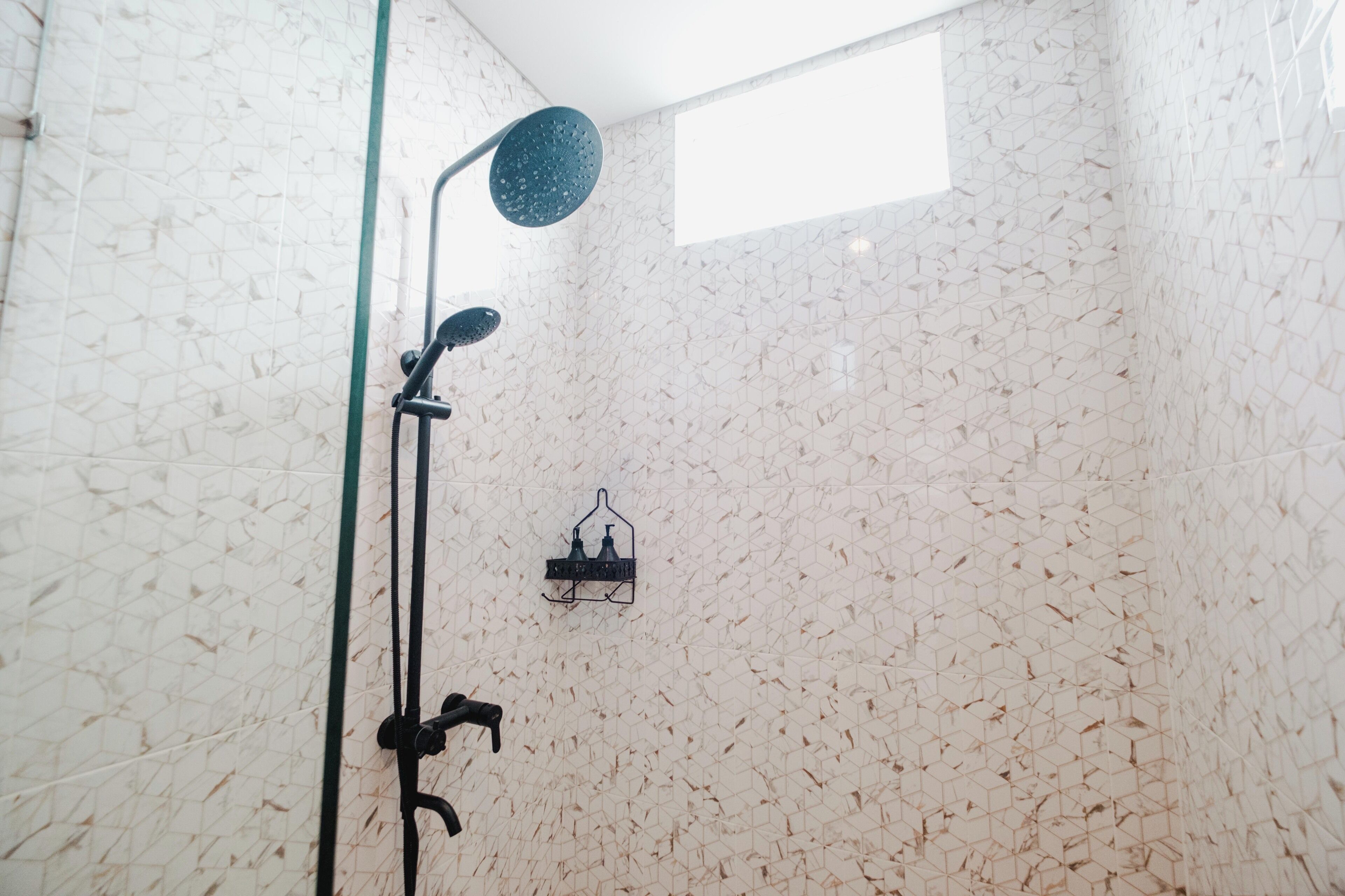 A shower with a rain showerhead and a wall-mounted soap dispenser.