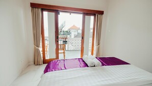 A hotel room with a bed, a view of the outside, and a balcony with a chair. - Turtle Shelter Guest House (Denpasar)