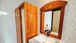 A bathroom with a wooden door, a white sink, a mirror, and a toilet paper roll. - Turtle Shelter Guest House (Denpasar)
