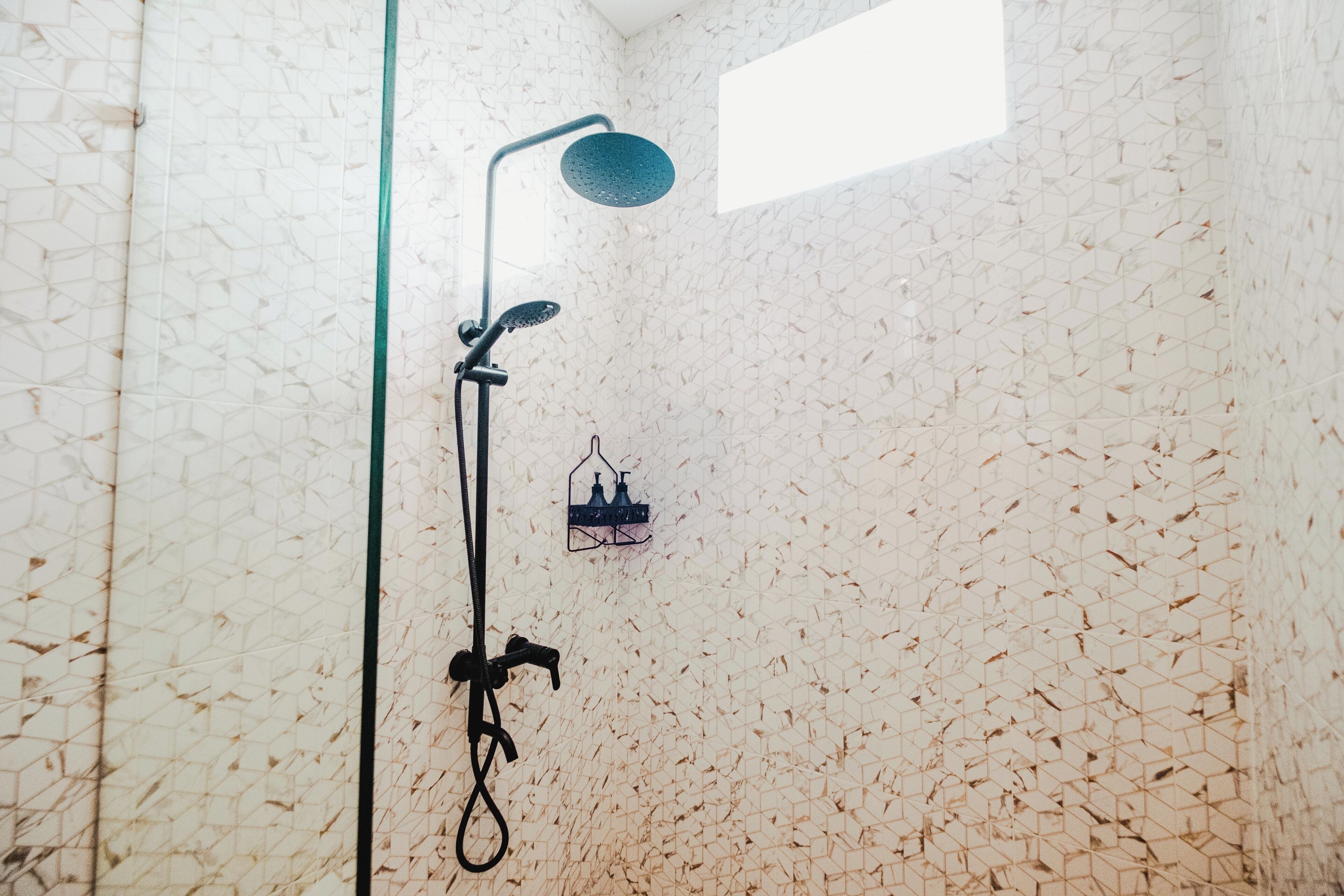 A shower with a geometric wall pattern, a handheld showerhead, and a wall-mounted faucet.