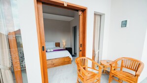 A hotel room with a wooden bed, a small table with chairs, and a view through an open door. - Turtle Shelter Guest House (Denpasar)