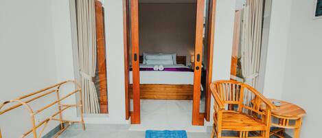 A room with a bed, a wooden chair, a small table, and a blue mat on the floor.
