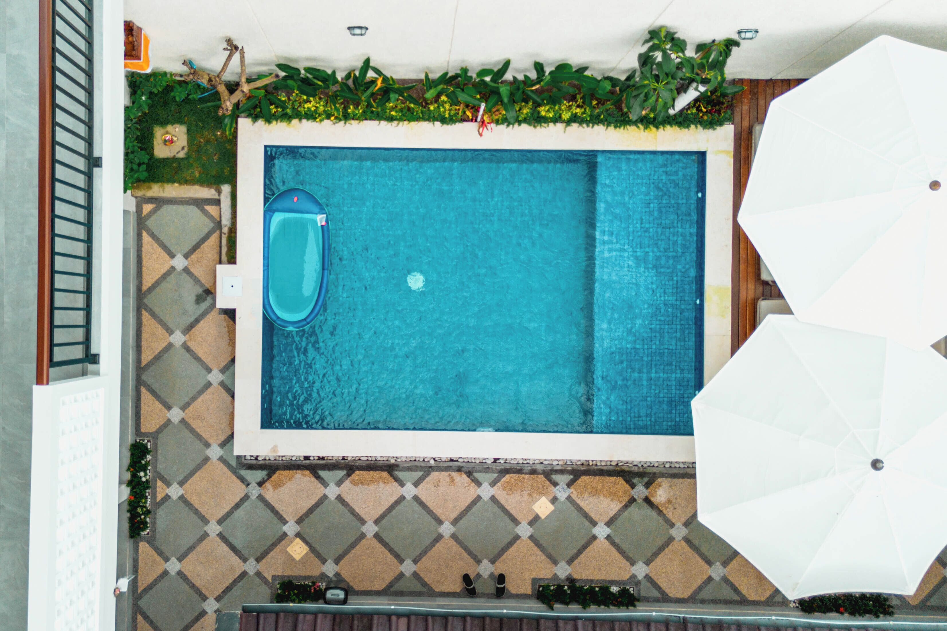 Una piscina en la azotea con vistas a la ciudad, rodeada por un patio empedrado y una sombrilla blanca.