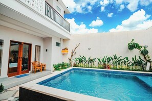 A modern building with a swimming pool, wooden chairs, and a balcony. - Turtle Shelter Guest House (Denpasar)