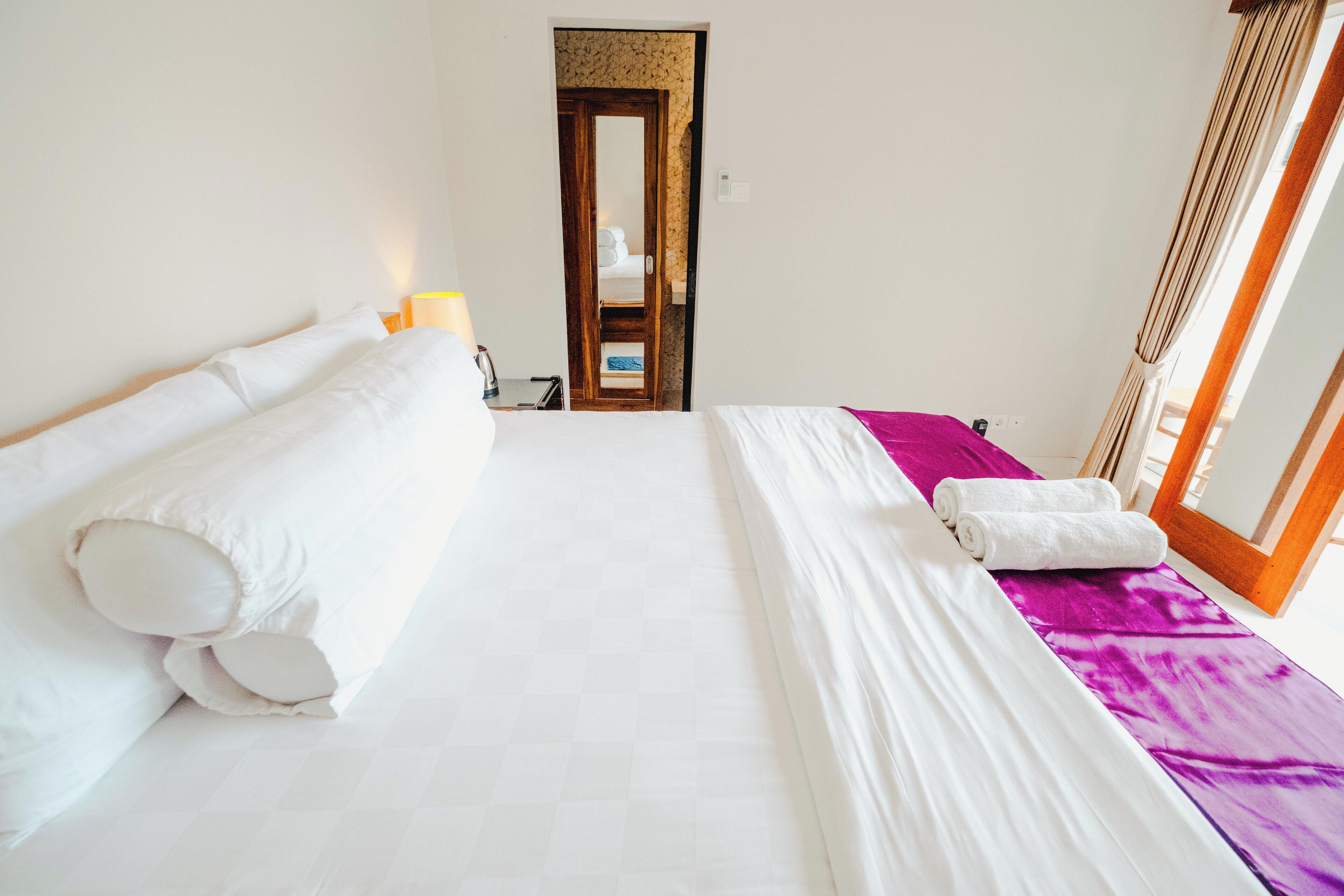 A hotel room with a large bed, a purple blanket, and a wooden door leading to a bathroom.