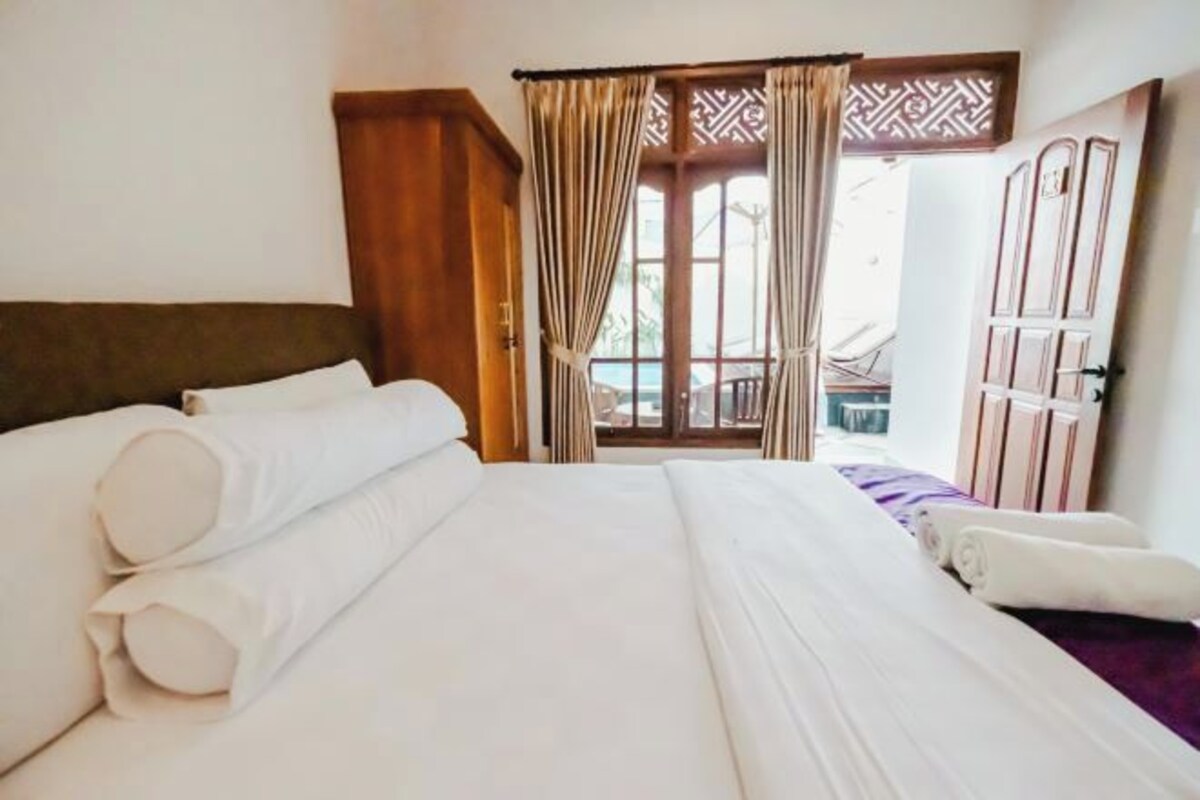 A hotel room with a large bed, a wooden headboard, a window with curtains, and a view of the outside.