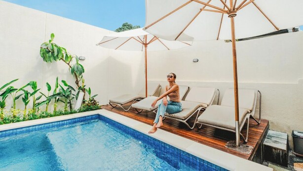A pool area with lounge chairs and umbrellas, surrounded by plants and a clear sky. - Turtle Shelter Guest House (Denpasar)