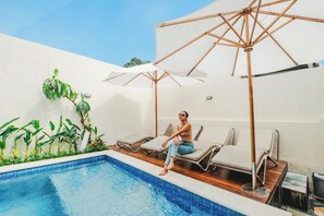 A pool area with lounge chairs and umbrellas, surrounded by plants and a clear sky. - Turtle Shelter Guest House (Denpasar)