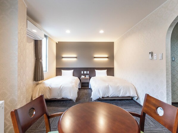 Habitación de hotel con dos camas, una mesa, sillas y un escritorio con teléfono.