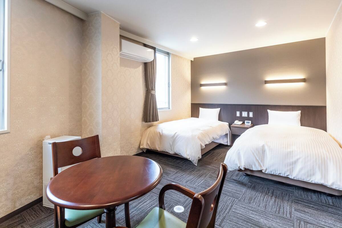 Ein Hotelzimmer mit zwei Betten, einem Esstisch und einem Stuhl.