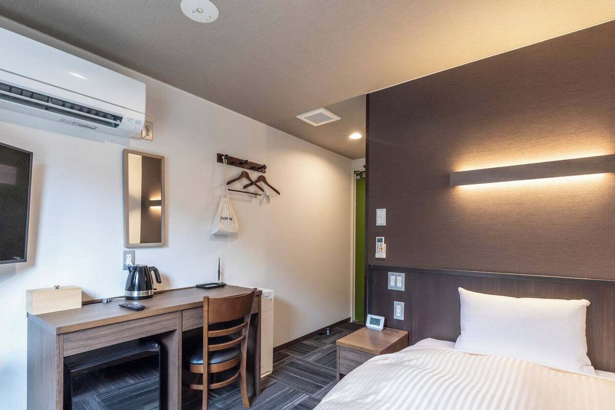 Ein Hotelzimmer mit einem Bett, einem Schreibtisch mit Stuhl, einer Kaffeemaschine, einem Fernseher und einem Wandheizkörper.
