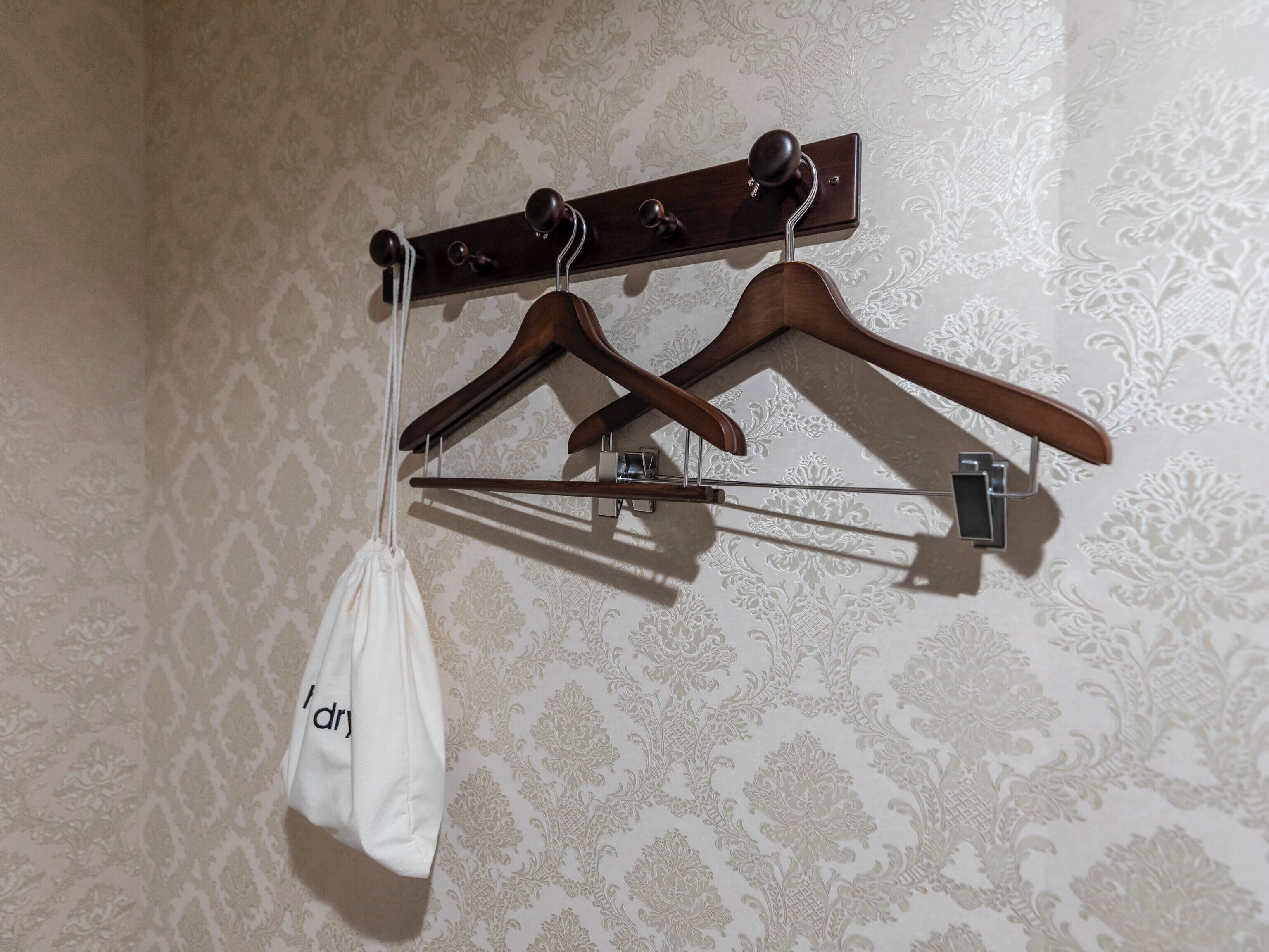 Un perchero de pared con tres perchas de madera y una bolsa blanca.