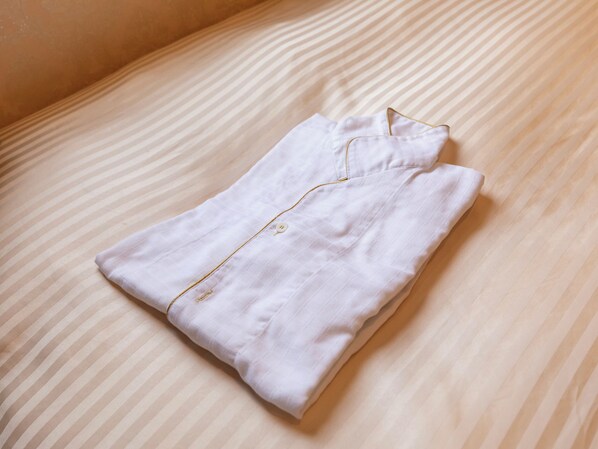 Una camisa blanca doblada con detalle dorado sobre una colcha a rayas.