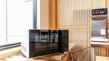 A modern kitchen with a black microwave oven on a wooden countertop, a coffee machine on a separate counter, and a window with blinds in the background.
