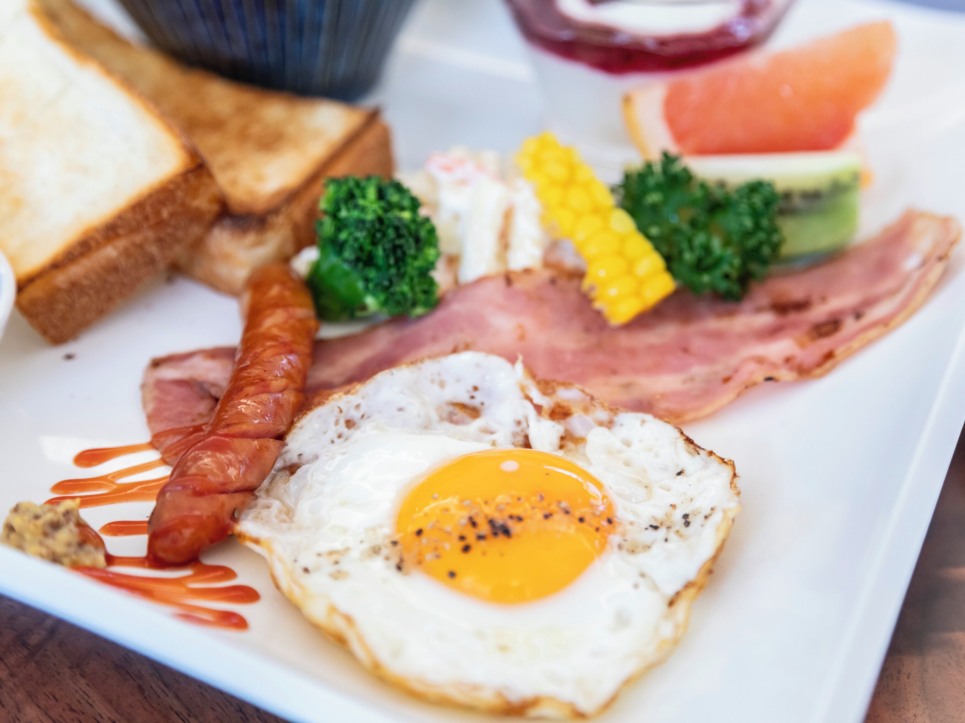 A breakfast plate with eggs, bacon, sausage, toast, and vegetables.
