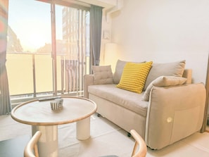 A modern living room with a sofa, a round coffee table, and a view through a large window.