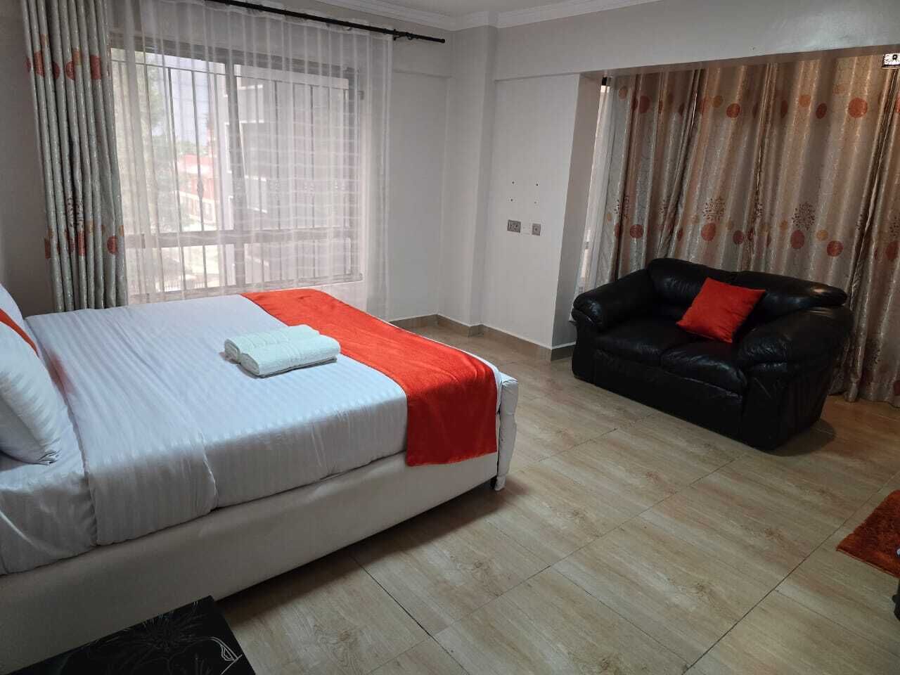 A bedroom with a bed, a black leather sofa, and a window with curtains.