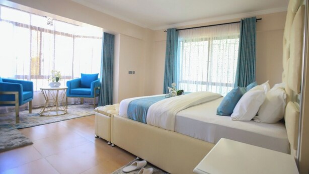 A hotel room with a large bed, a small table, a sofa, and a window with curtains. - Shawmut Suites Nakuru (Nakuru)