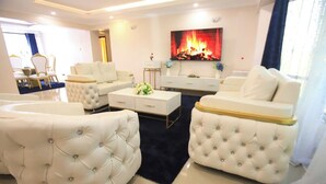 A modern living room with a fireplace, white furniture, and a dining area in the background. - Shawmut Suites Nakuru (Nakuru)