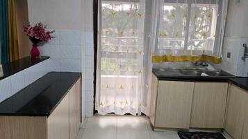 A kitchen with a black countertop, wooden cabinets, a white tiled floor, a sink, and a window with a curtain.