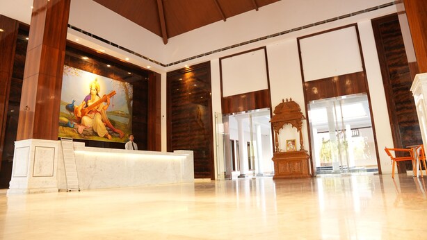 A spacious lobby with a reception desk, a large mural, and a view of the outside. - Lords Hrim Akshara Resort (Mudhol)
