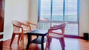 Una habitación con ventilador de techo, un ventanal con persianas y una mesa con sillas.