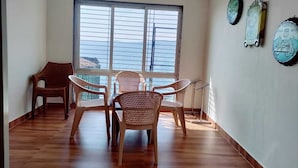 Una habitación con un ventanal grande, piso de madera y tres sillas de mimbre.