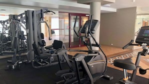 Un gimnasio con diferentes máquinas de ejercicio, un espejo grande en la pared y una puerta que da a otra habitación.