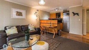 Una sala moderna con una mesa de centro de vidrio, un sofá de cuero oscuro, un área de comedor con una mesa y sillas de madera, y una cocina con refrigerador y microondas.
