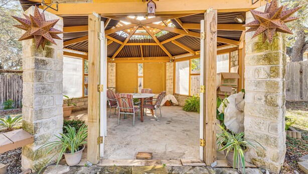 Ein überdachter Patio-Bereich mit Holztisch und -stühlen, Steinpfeilern und Kübelpflanzen.