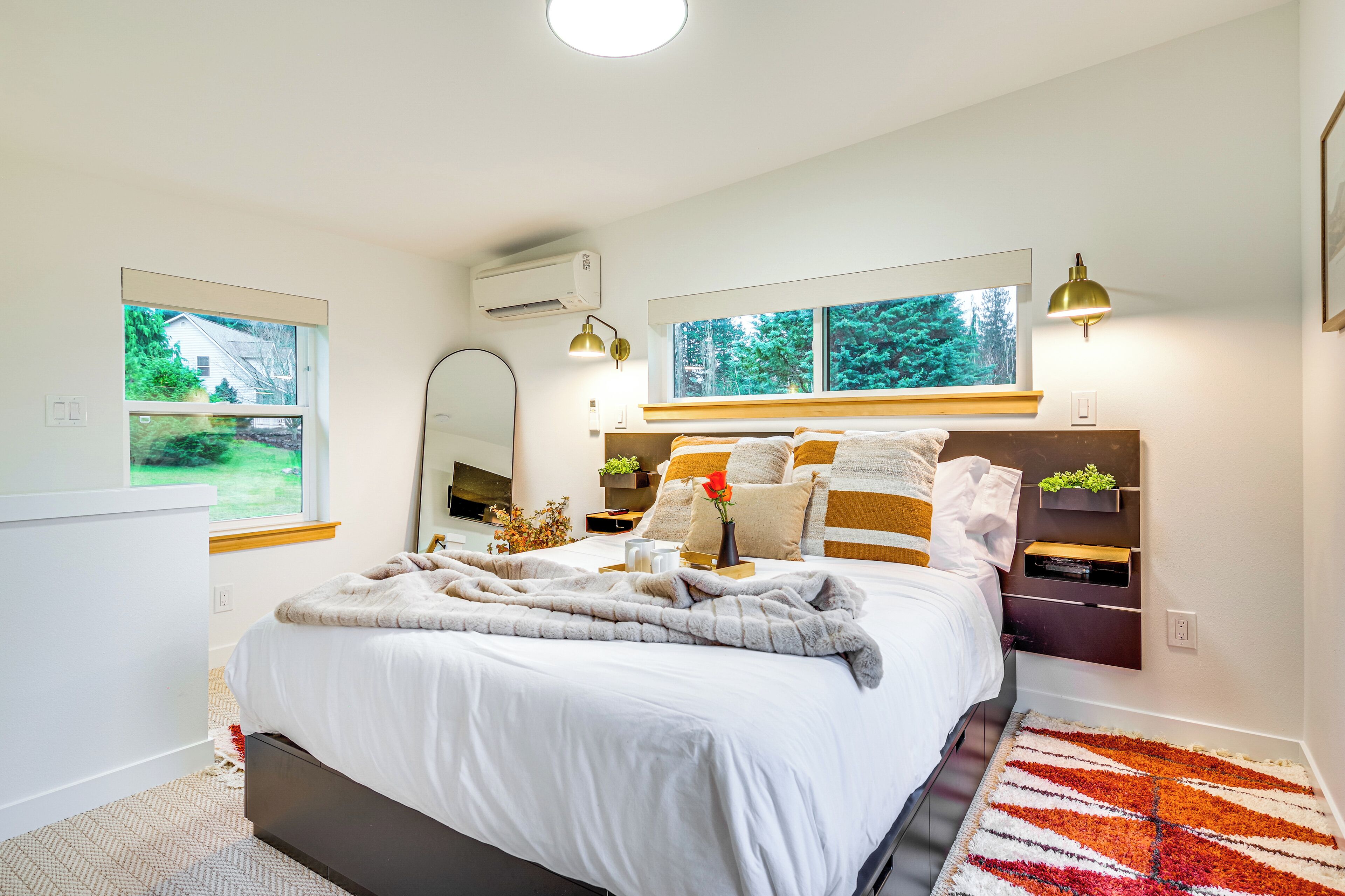 Un dormitorio moderno con una cama grande, mesitas de noche, un espejo y una ventana con vistas a zonas verdes.