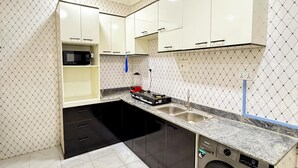 Cocina compacta con armarios blancos, microondas integrado, lavamanos y lavadora.