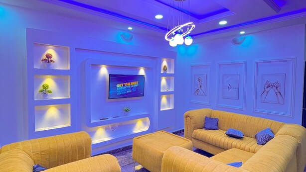 Un salón moderno con un televisor de pantalla plana grande, sofás amarillos e iluminación azul en el techo.