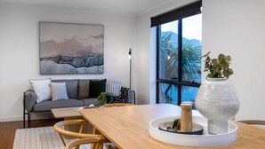 A modern living room with a wooden dining table, a grey sofa, and a large window with a view of palm trees. - Lipscombe Mt Wellington view luxury house (HOBART)