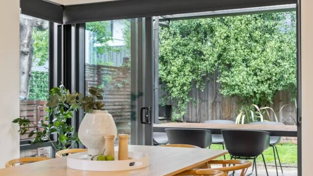 A modern dining area with a large table and chairs, a vase with plants, and a view of a lush garden through large glass doors. - Lipscombe Mt Wellington view luxury house (HOBART)