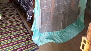 Una habitación con una cama bajo una mosquitera, cabecera de madera, alfombra estampada y techo rústico de paja.