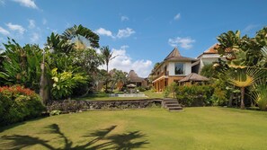 A tropical resort with a swimming pool, lush greenery, and multiple buildings with distinct architectural styles.