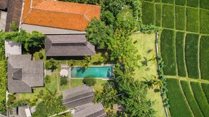 Vue aérienne d’une propriété résidentielle dotée d’une piscine, d’une végétation luxuriante et de champs en terrasses.