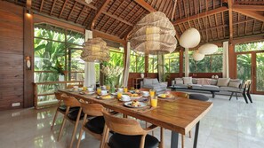 A spacious dining area with a long wooden table, surrounded by chairs, and a modern sofa in the background. - Alea Estate by Villa Finder (Kerobokan)