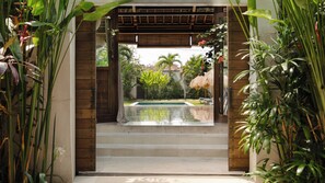 Área de piscina com escadas que levam à água, cercada por vegetação exuberante e uma pérgola de madeira.